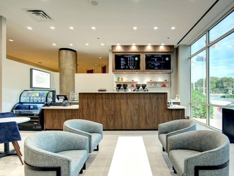 A modern reception area with a wooden counter, two grey armchairs, a coffee machine, and a large window offering a view of the parking lot.