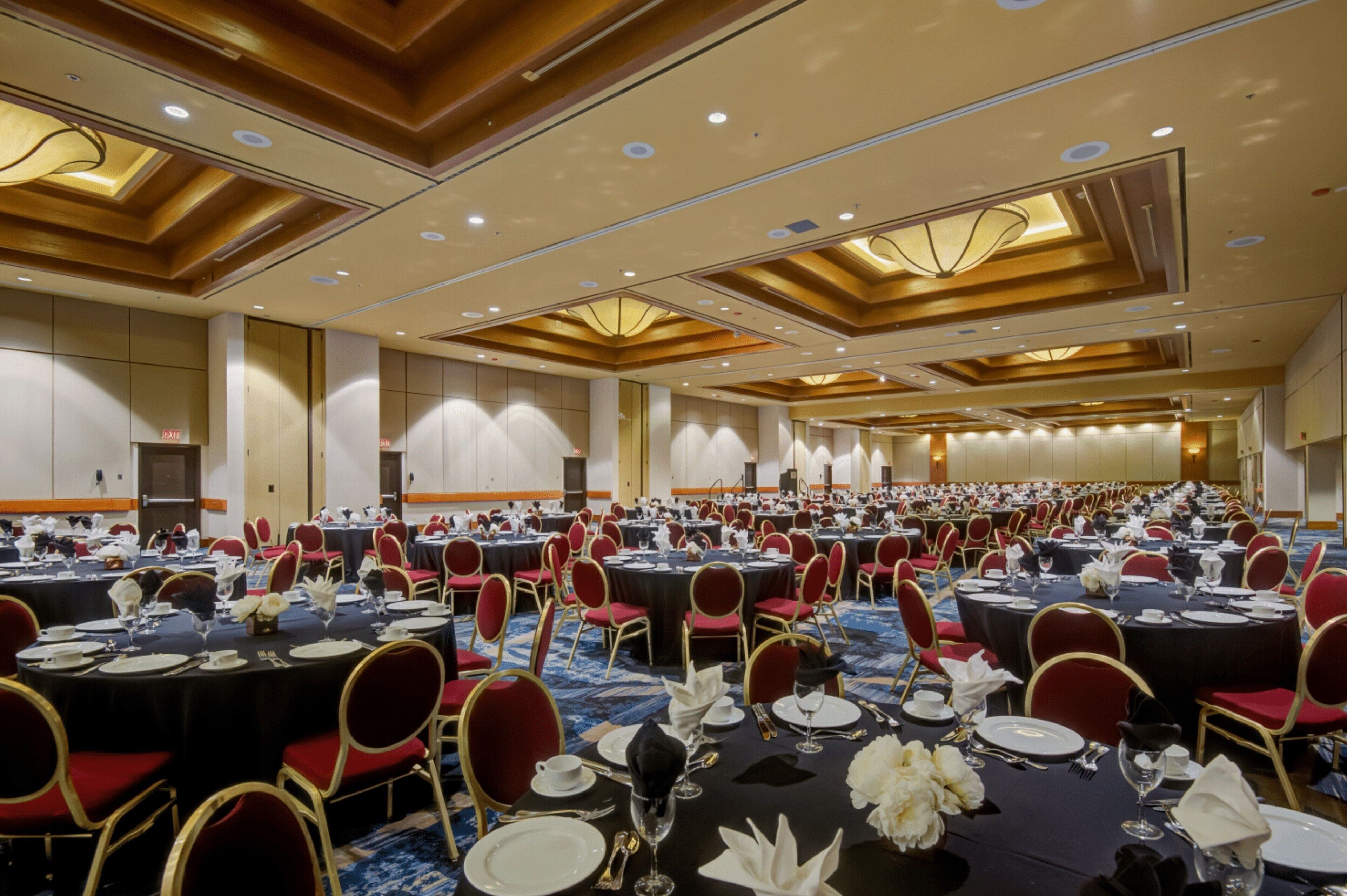 A large banquet hall with round tables set for dining, red chairs, and a blue carpet.