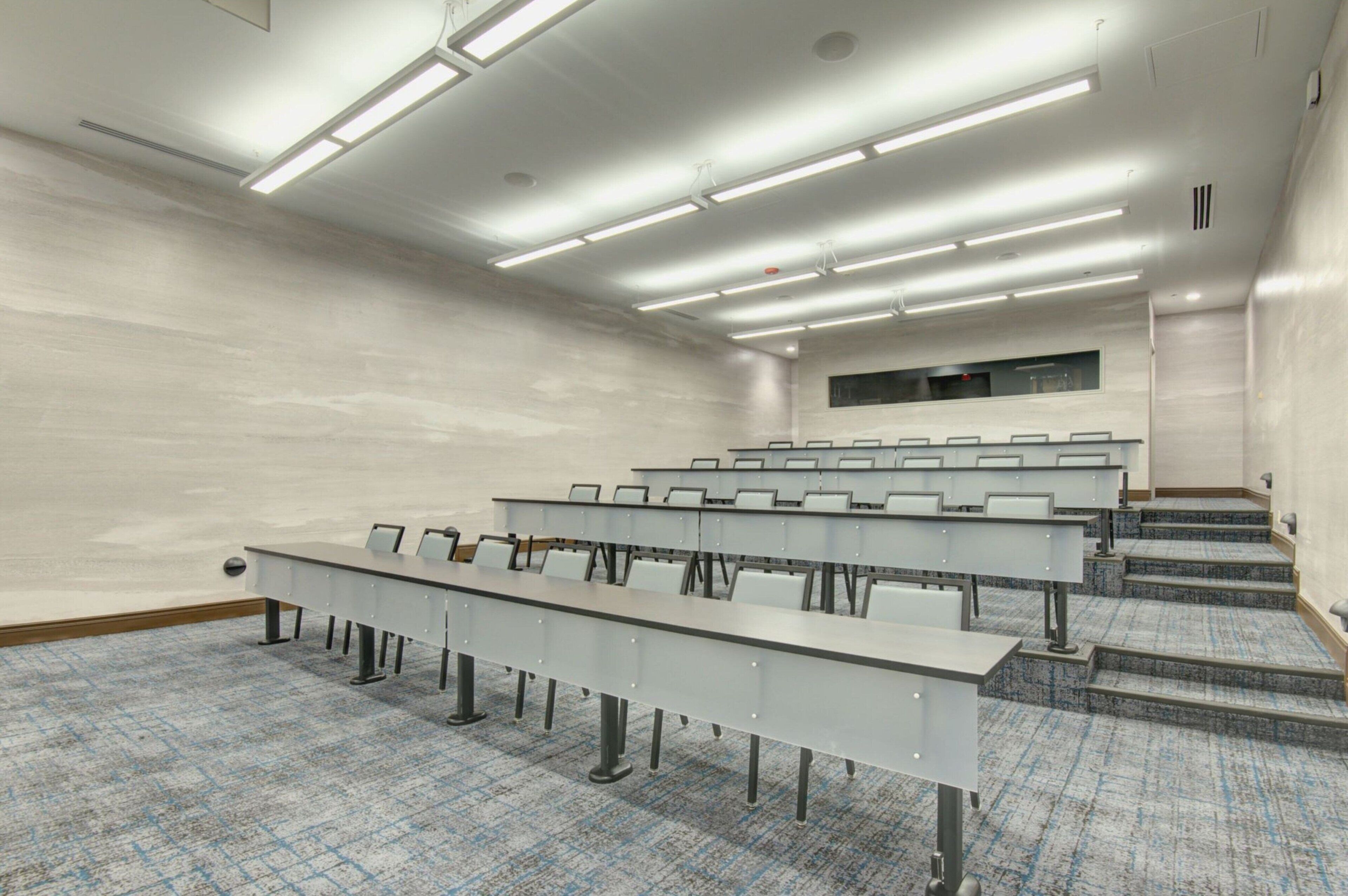 Une salle de conférence avec une longue table, des rangées de chaises, un sol recouvert de moquette et un escalier menant à un niveau supérieur.