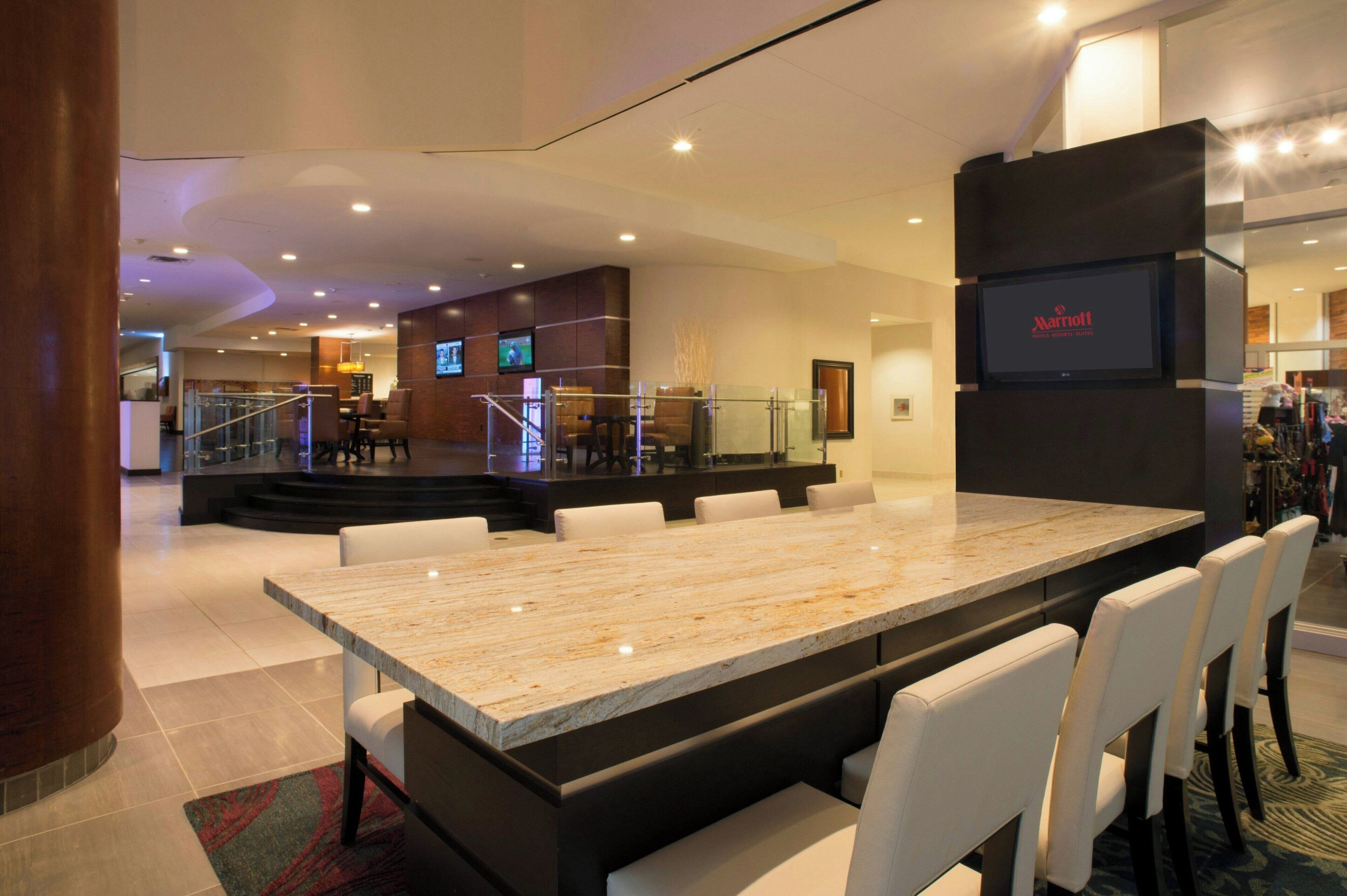 Un moderno vestíbulo de hotel con un amplio mostrador de recepción de mármol, zona de estar y una pantalla mostrando el logotipo de Marriott.