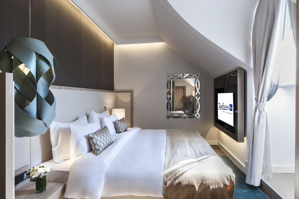 Una habitación de hotel moderna con una cama grande, un televisor montado en la pared y un espejo decorativo.