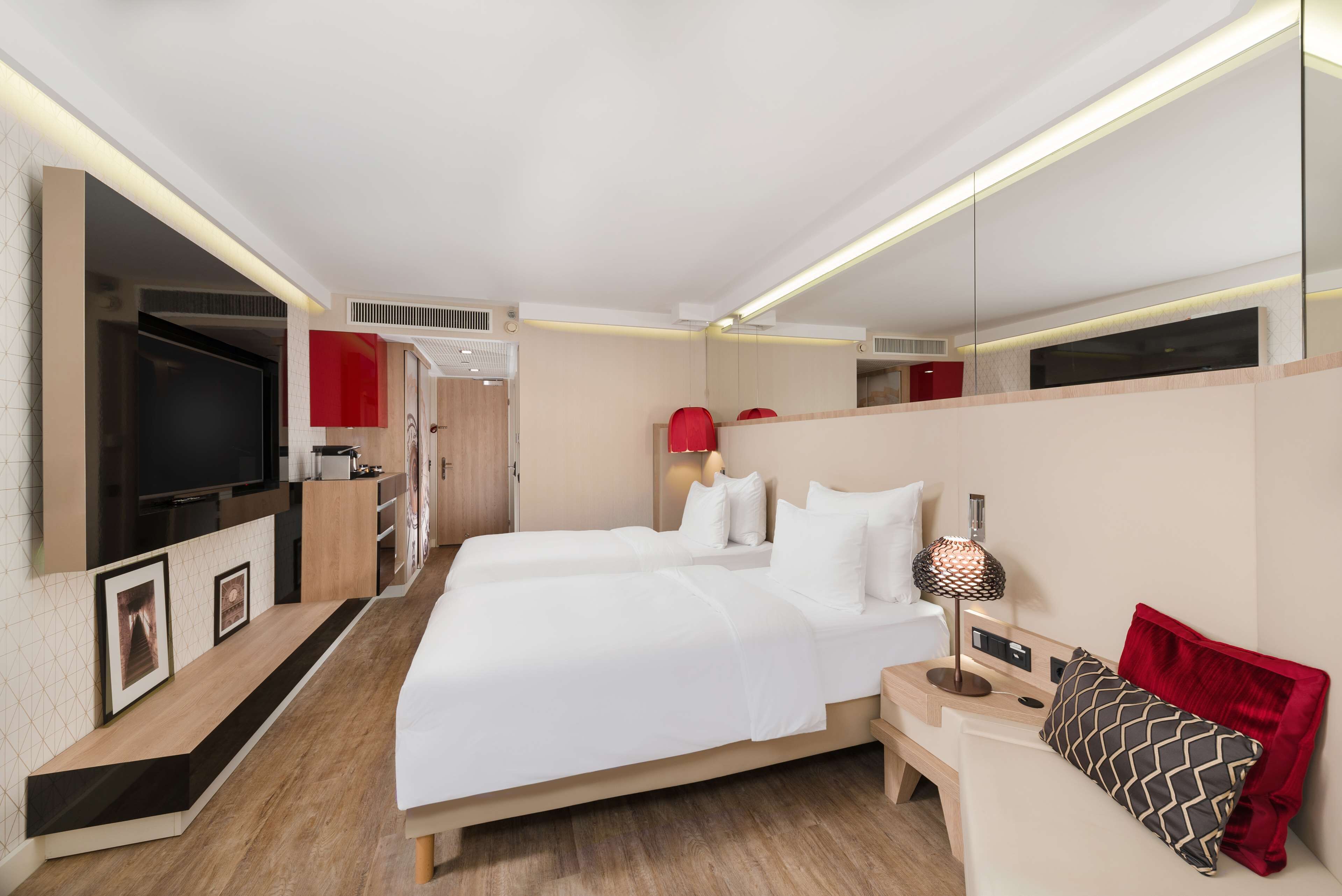Une chambre d’hôtel moderne avec deux lits, une télévision, un bureau et un mur d’accent rouge.