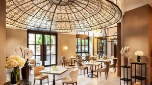 A modern interior with a large glass dome ceiling, tables, chairs, and decorative vases. - Radisson Blu Beke Hotel, Budapest (Budapest)