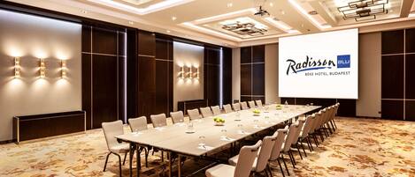 Een vergaderzaal met een lange tafel, stoelen en een projectiescherm waarop het Radisson logo staat.