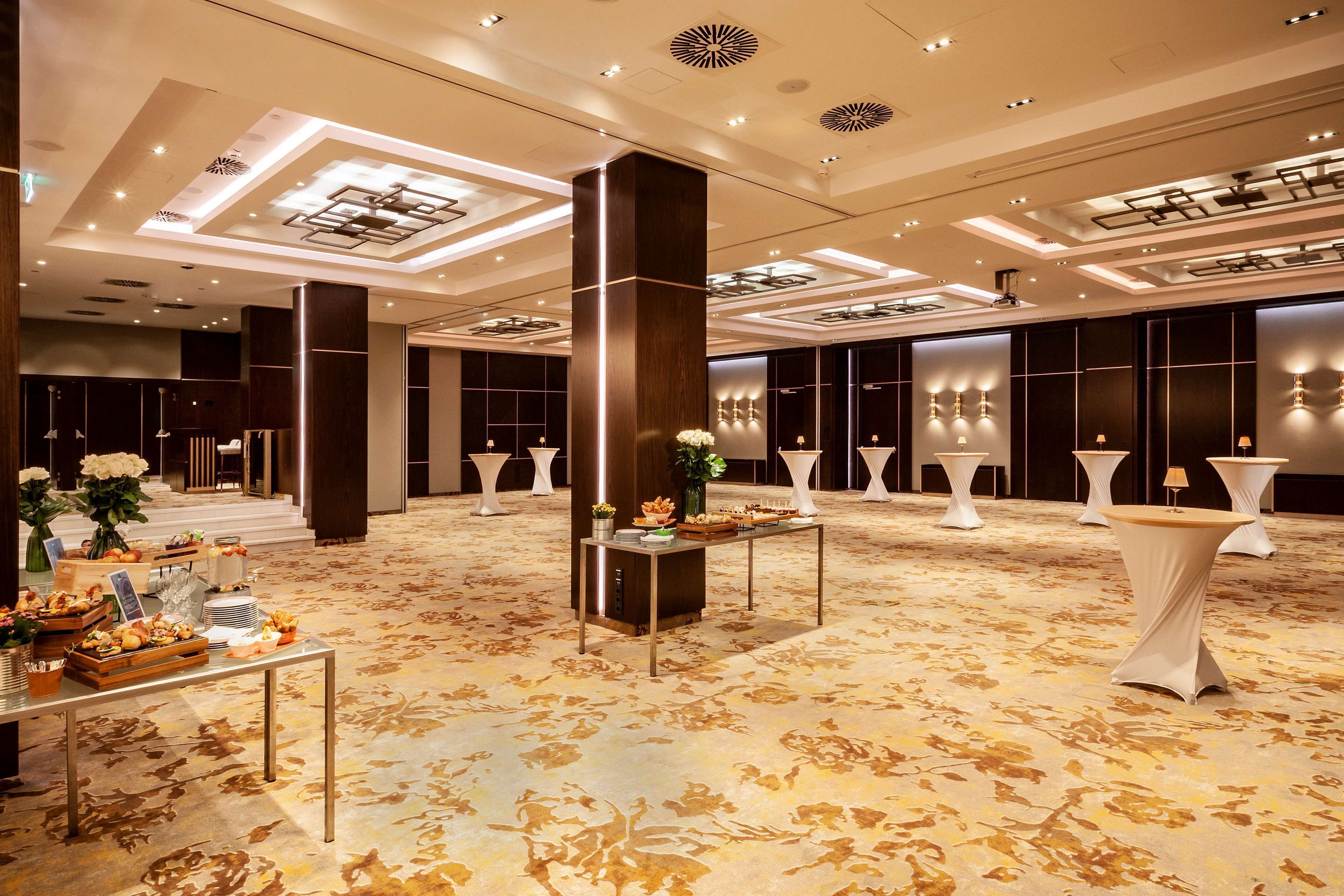 A spacious hotel lobby with a floral carpet, a central reception desk, and modern lighting fixtures.