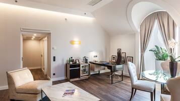 A modern living room with a glass table, comfortable seating, a built-in kitchen, and a large window with curtains.