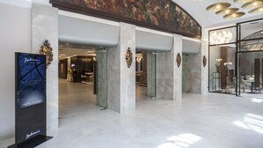 A spacious lobby with marble columns, a large painting above the reception, and a modern chandelier. - Radisson Blu Beke Hotel, Budapest (Budapest)