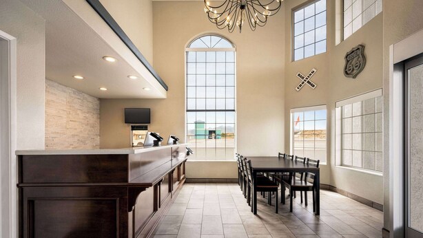 A modern kitchen with a long counter, a dining area with a table and chairs, and a large window providing a view of the outside. - Baymont by Wyndham Kingman (Kingman)