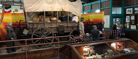 Eine historische Ausstellung mit einem Wagen, Holzfässern und einer Vitrine mit verschiedenen Gegenständen.