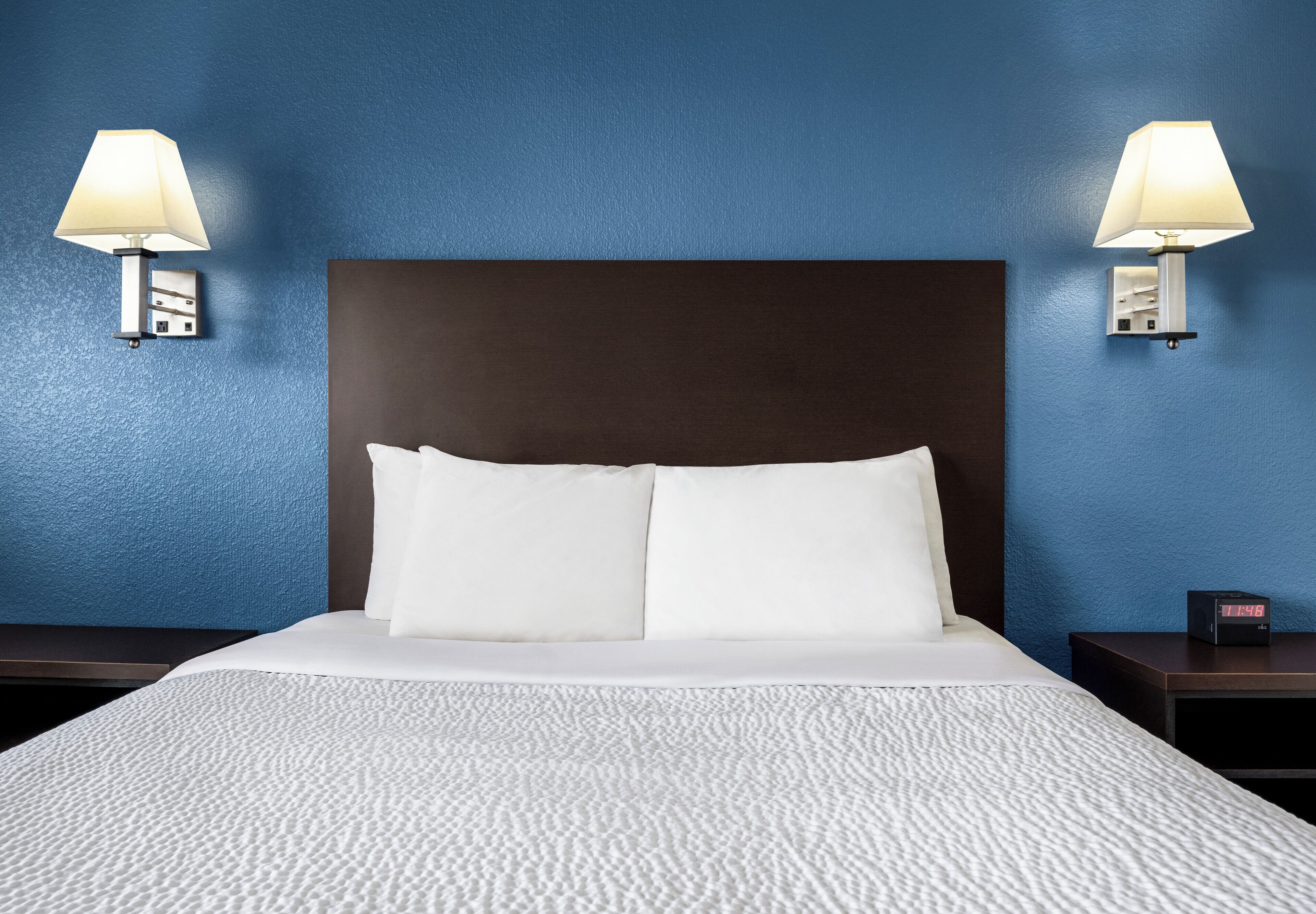 A hotel room with a large bed, two bedside lamps, a nightstand, and a digital clock.