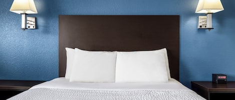 Et hotelværelse med en stor seng, to sengeborde, lamper og et digitalt ur.