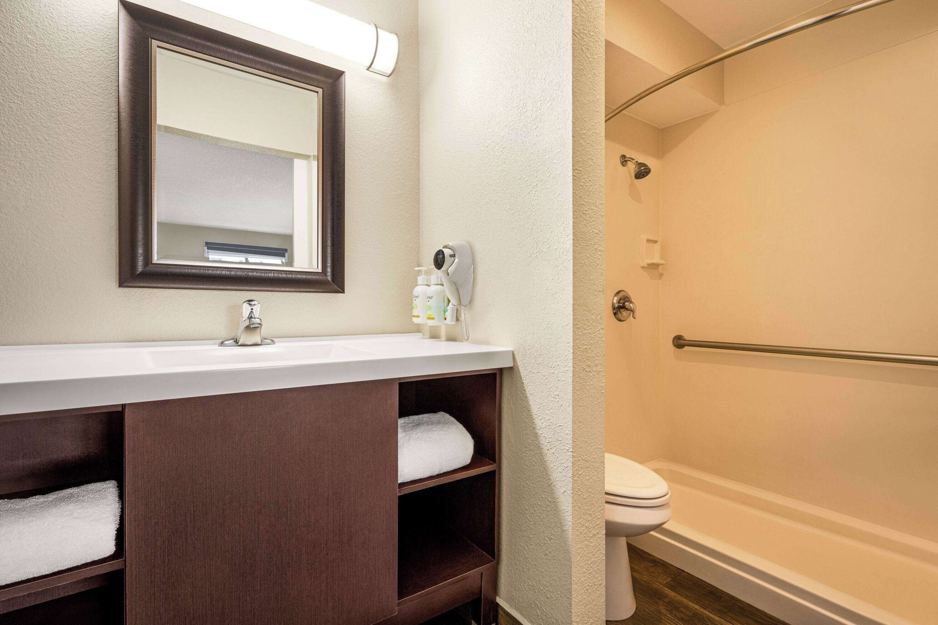 A bathroom with a white sink, dark wooden vanity, a mirror, a towel rack, a toilet, and a shower with a glass door.
