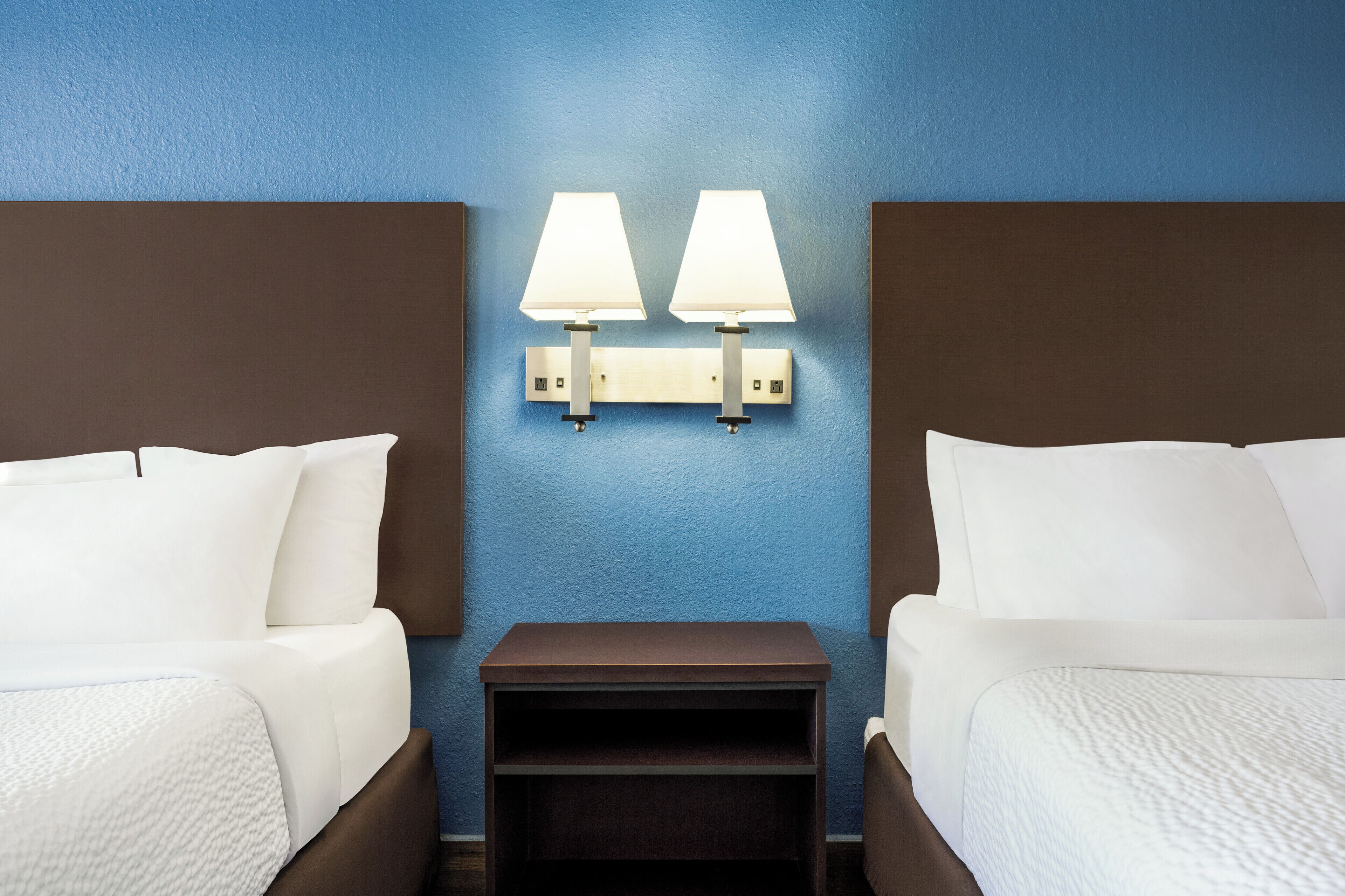 Une chambre d’hôtel avec deux lits, une table de chevet et des lampes fixées au mur.