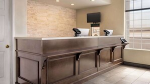 A reception area with a stone wall, a flat-screen TV, a phone, and a window with blinds. - Baymont by Wyndham Kingman (Kingman)