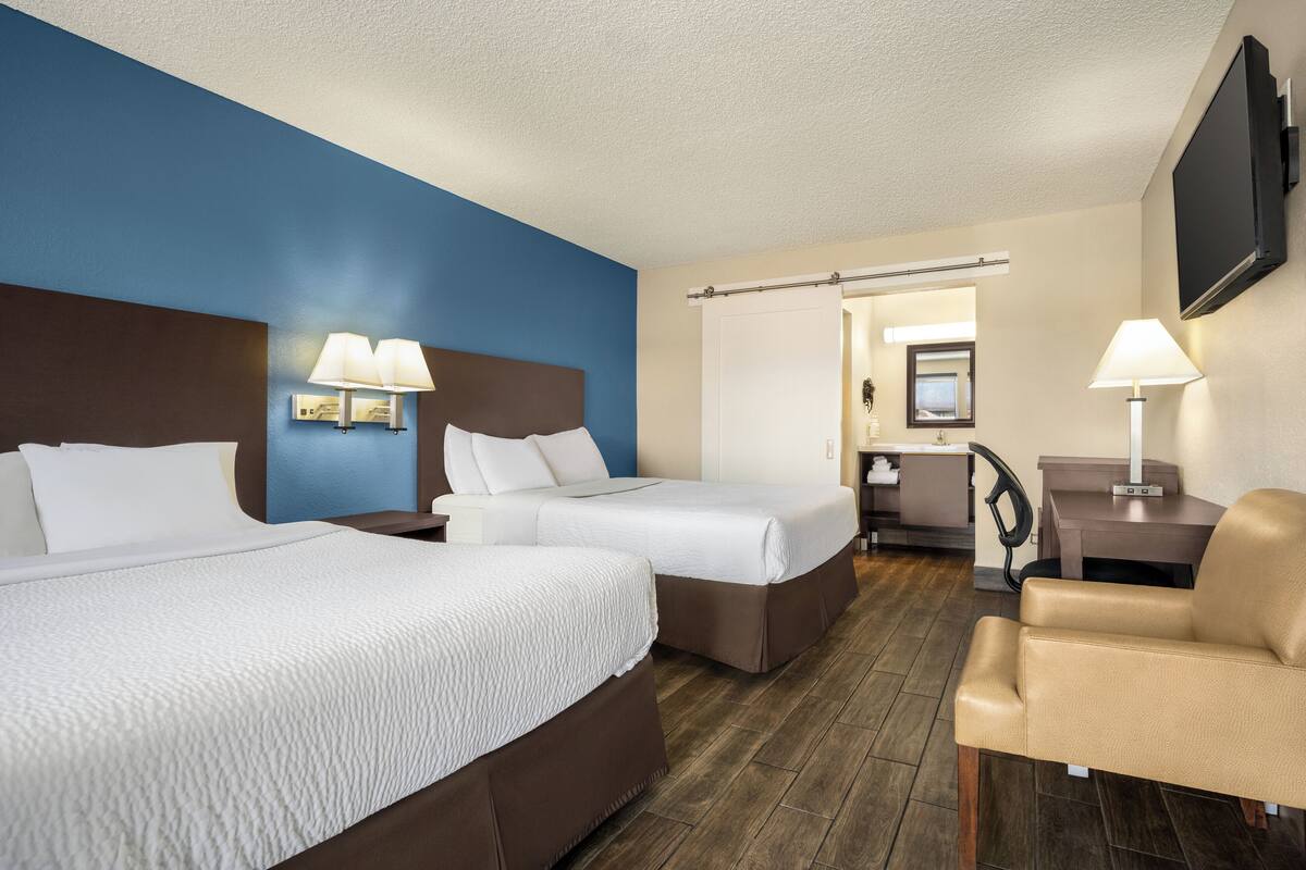 A hotel room with two beds, a desk, a chair, and a TV.