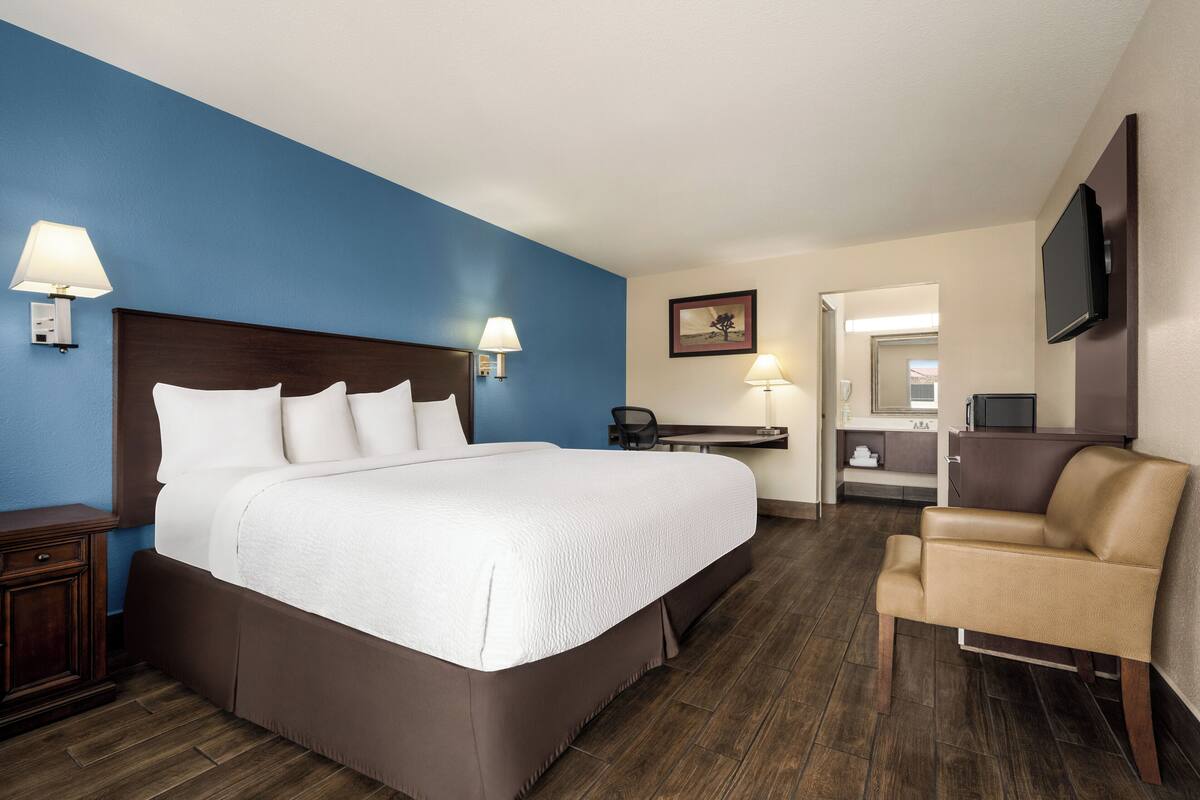 A hotel room with a large bed, bedside lamps, a desk with a chair, a TV, and a small sofa.