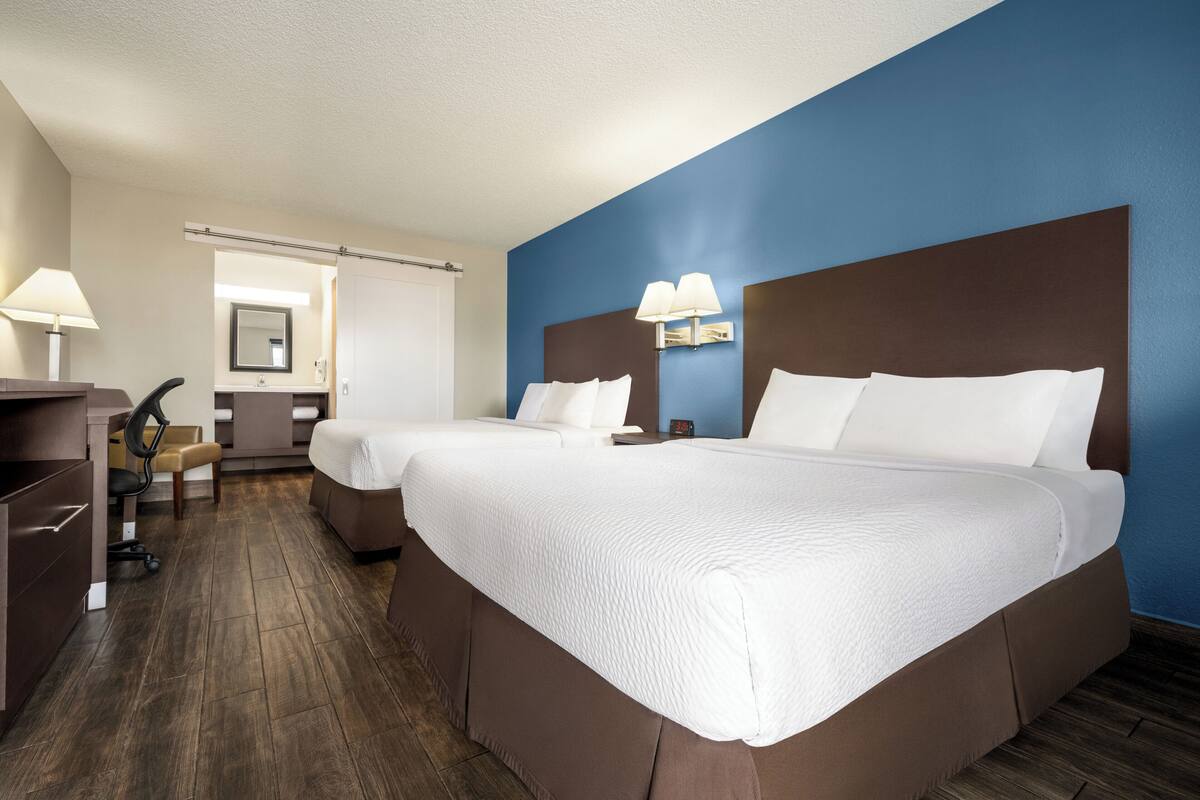A hotel room with two beds, a desk, and a chair.