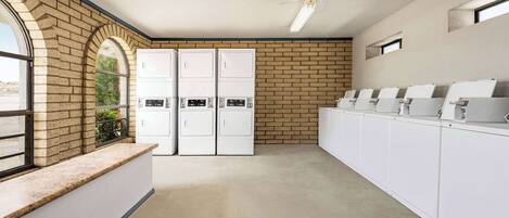A laundry room with a brick wall, ceiling fans, and a row of white appliances.