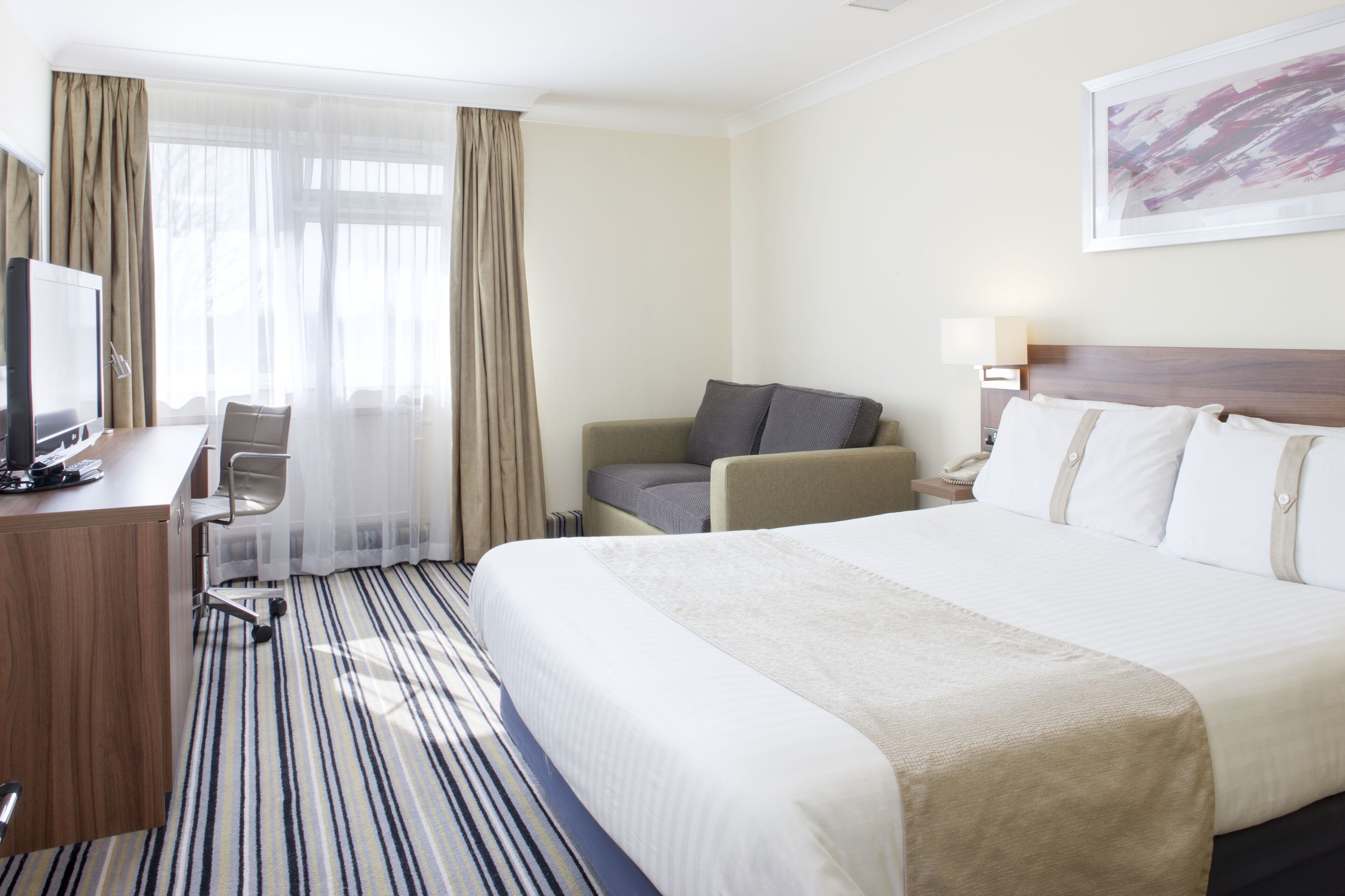 Una camera d'albergo con un letto grande, una scrivania con un computer, una sedia e una finestra con tende.