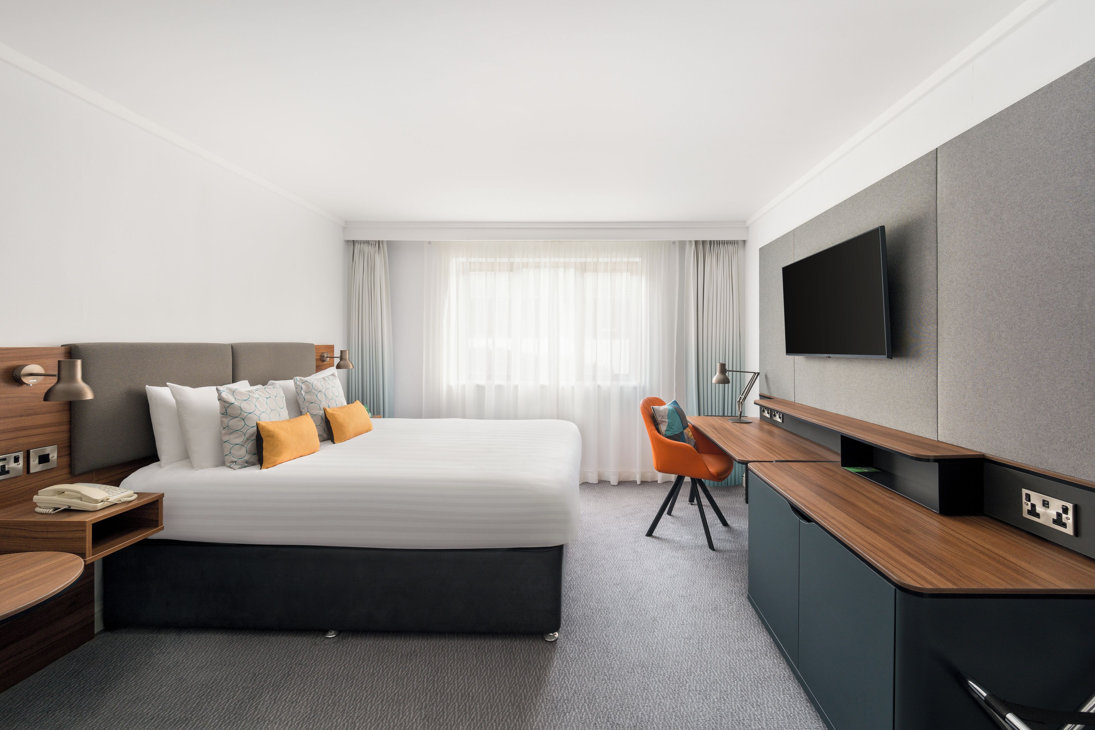 A hotel room with a bed, a desk, a television, and a window with curtains.