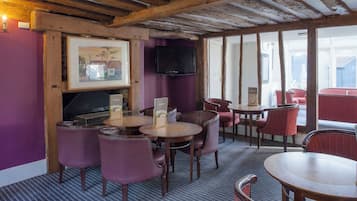 Un restaurante con vigas de madera, paredes moradas y un televisor en la pared. Hay mesas y sillas para comer.