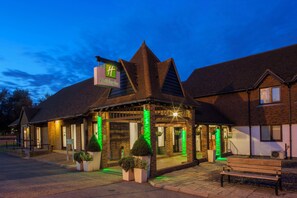 A Holiday Inn with a traditional architectural style, featuring a prominent sign, a covered entrance, and a bench in front.