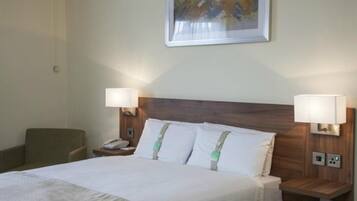 A hotel room with a bed, two bedside lamps, a chair, a nightstand, and a painting on the wall.