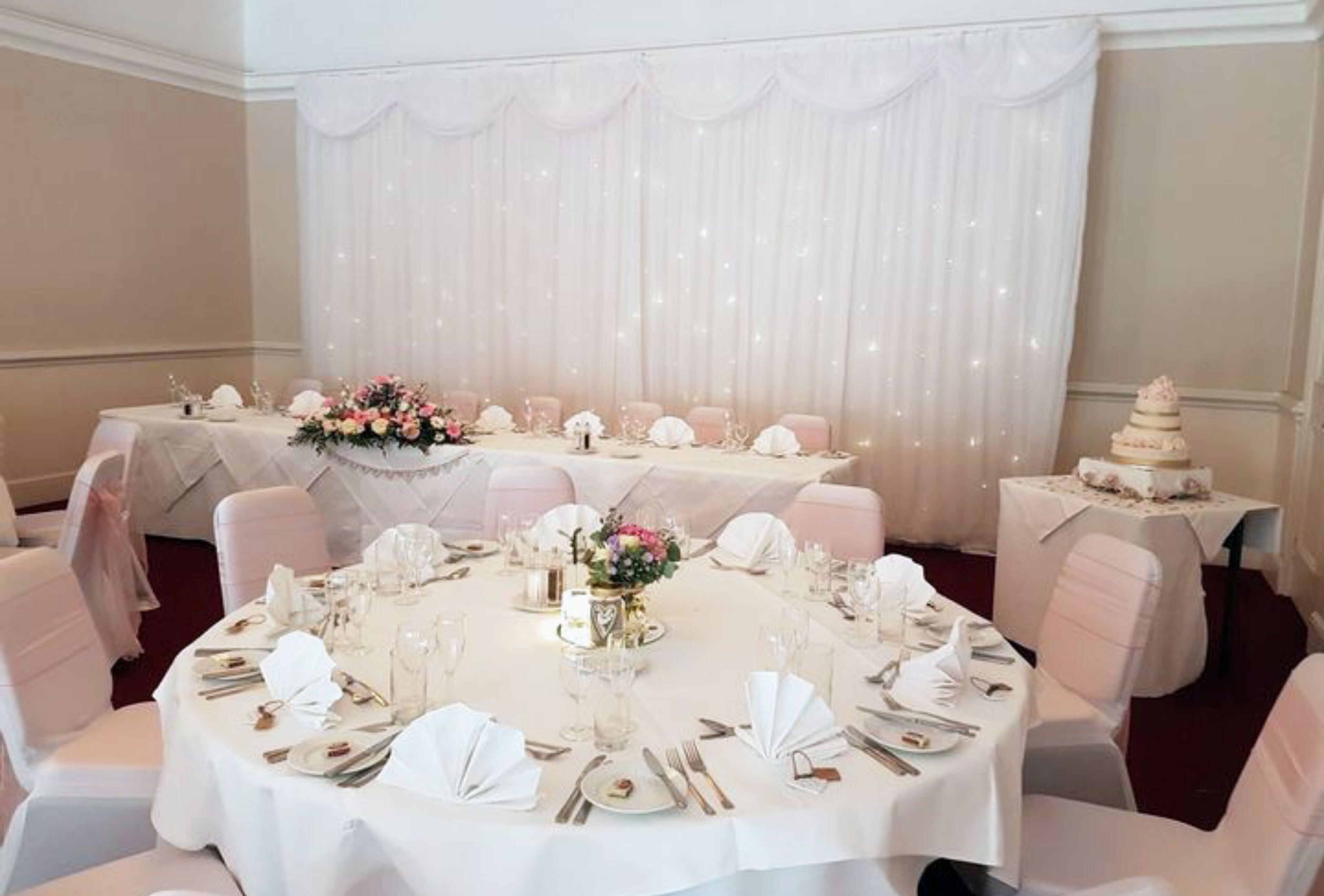 A banquet hall with round tables set for a formal event, featuring white tablecloths, floral centerpieces, and neatly arranged cutlery.