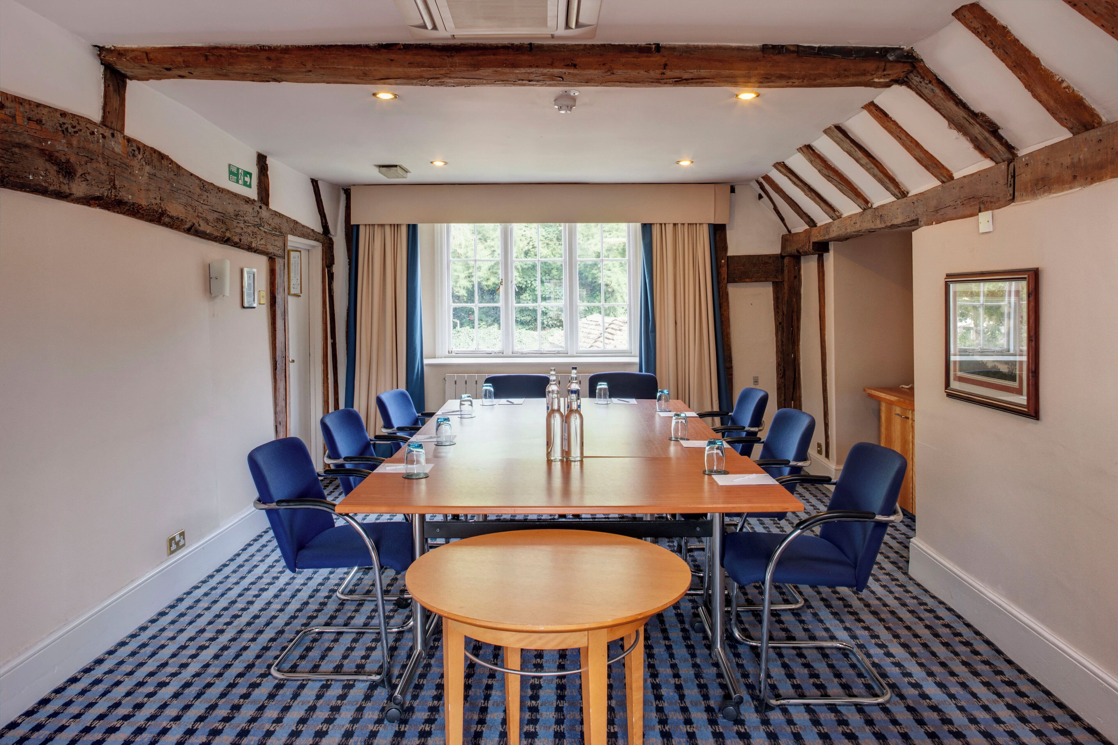 A conference room with a long table, blue chairs, and a window with curtains.