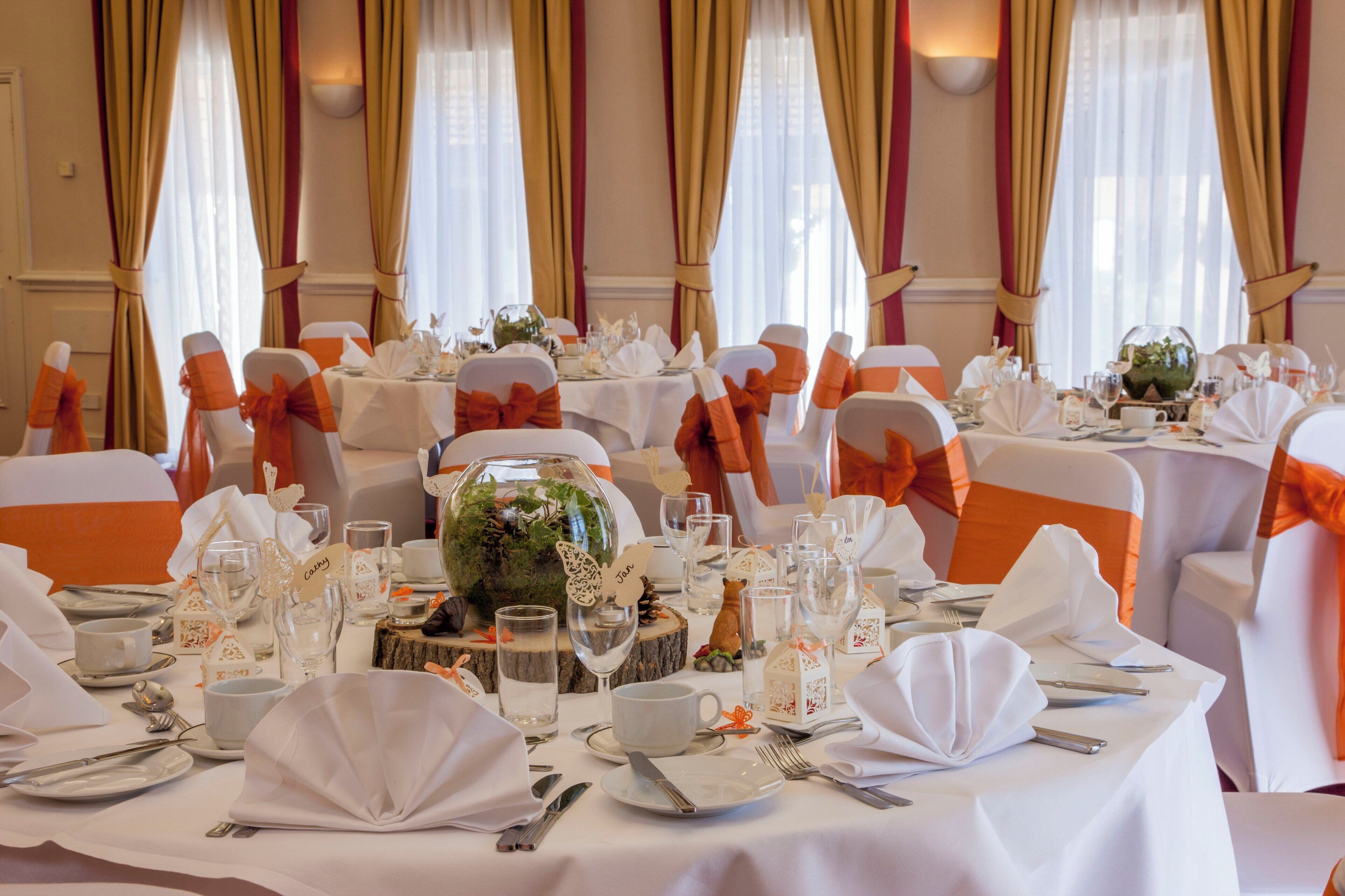 A banquet hall with round tables set for a formal event, featuring white tablecloths, neatly arranged cutlery, and glassware.