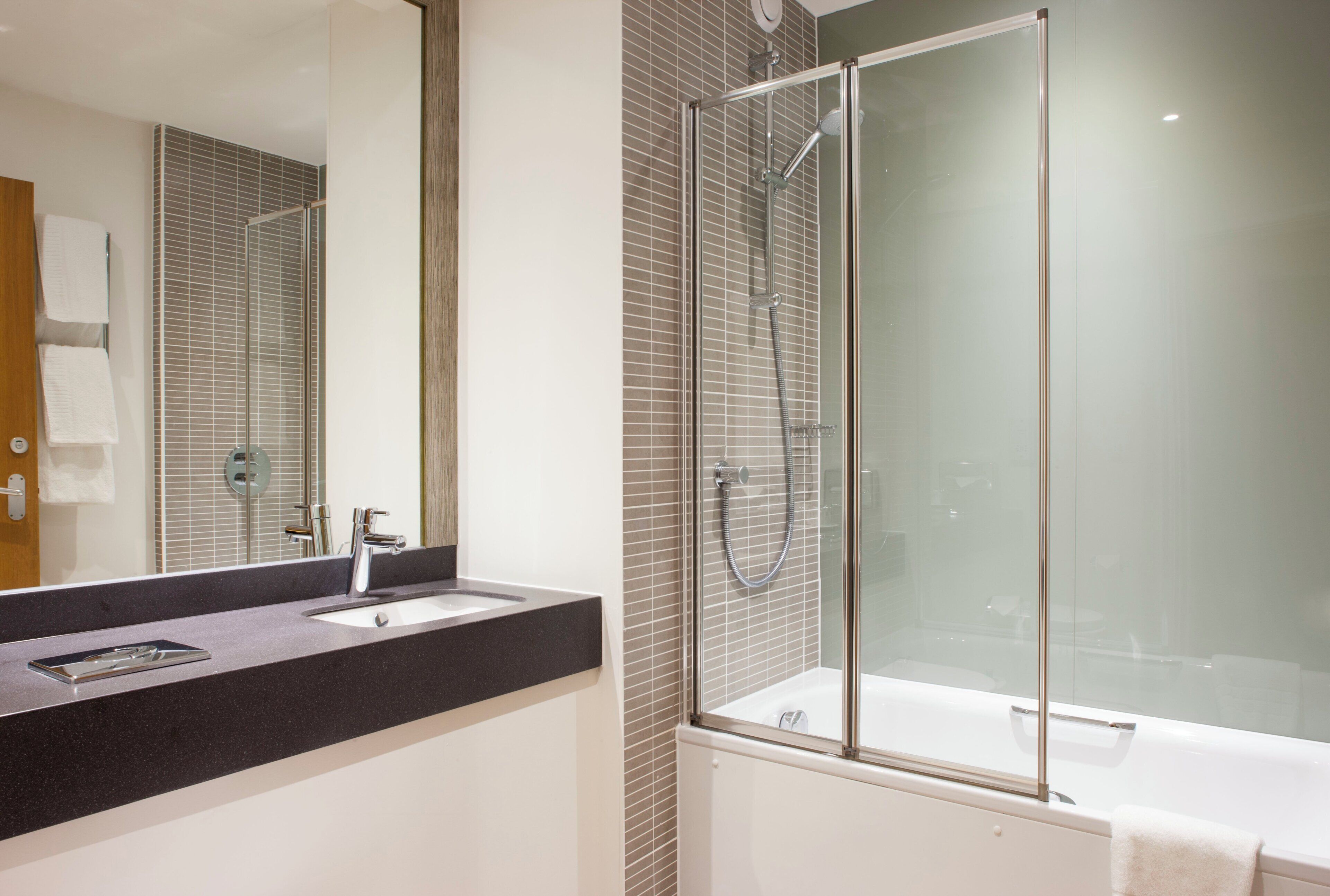 A modern bathroom with a glass-enclosed shower, a sink with a mirror, and a bathtub.
