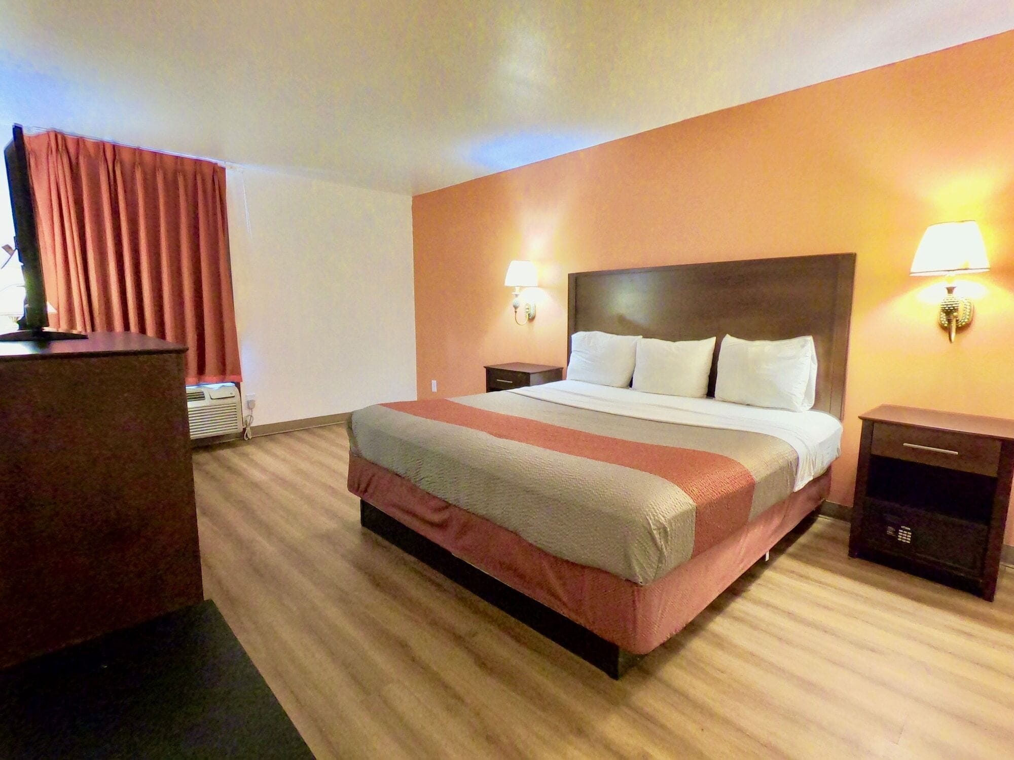 A hotel room with a large bed, two bedside tables, a desk, and a lamp.