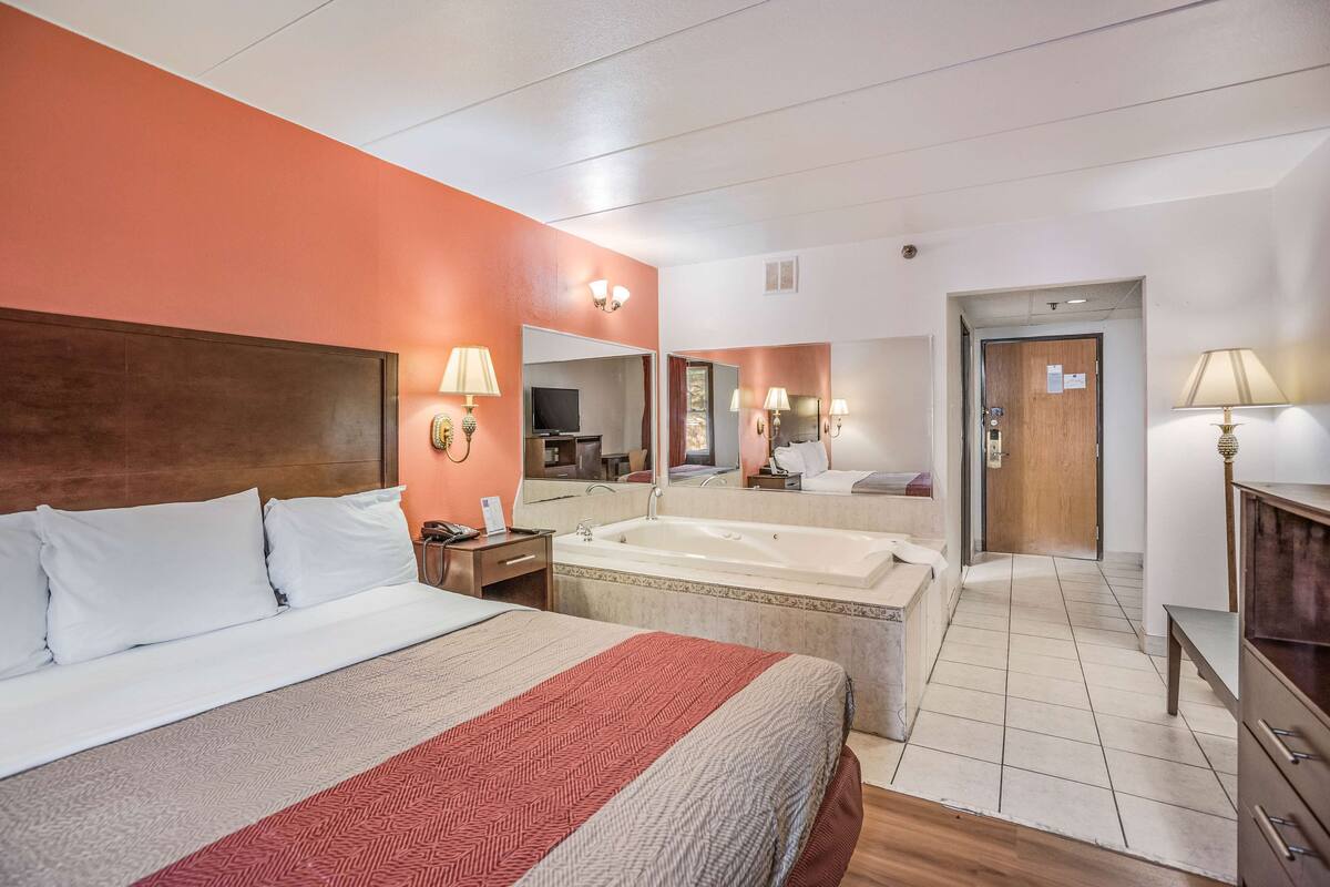 Ein Hotelzimmer mit einem großen Bett, einem separaten Badezimmer mit einer Badewanne und einem Spiegel, der den Raum widergibt.