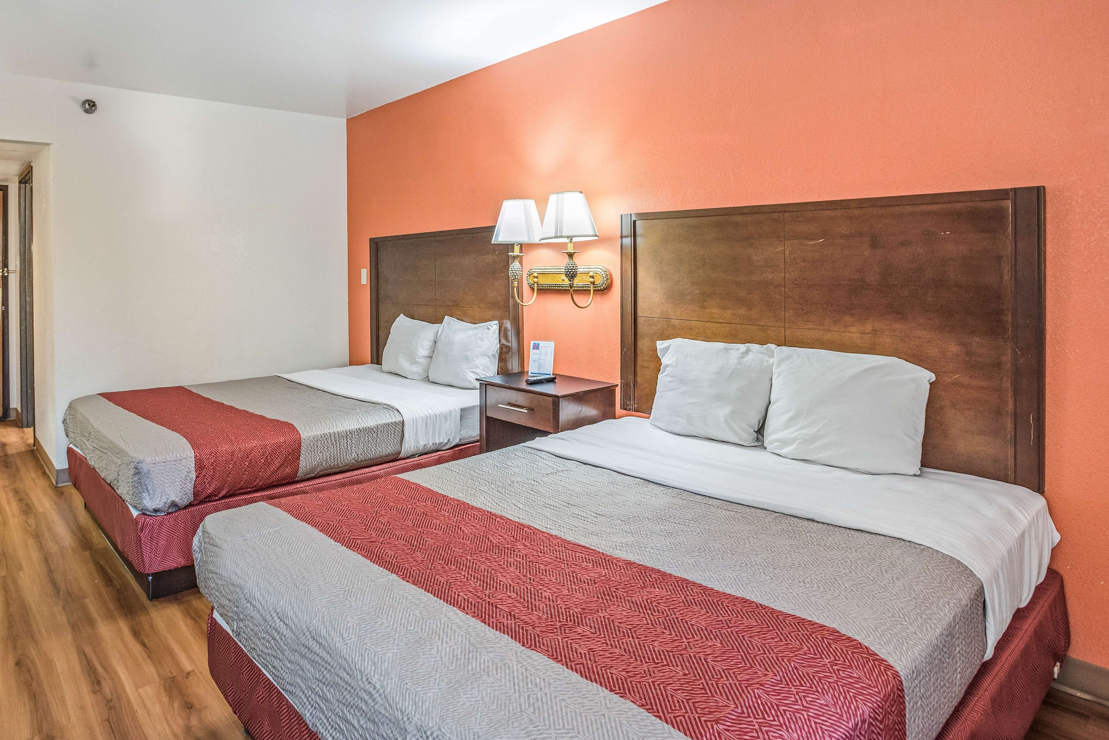 Une chambre d’hôtel avec deux lits, chacun recouvert d’une couvre-lit à motifs rouges et gris, dotés de têtes de lit en bois et d’une table de chevet avec une lampe placée entre les deux.