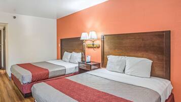 Une chambre d’hôtel avec deux lits, chacun recouvert d’une couvre-lit à motifs rouges et gris, dotés de têtes de lit en bois et d’une table de chevet avec une lampe placée entre les deux.