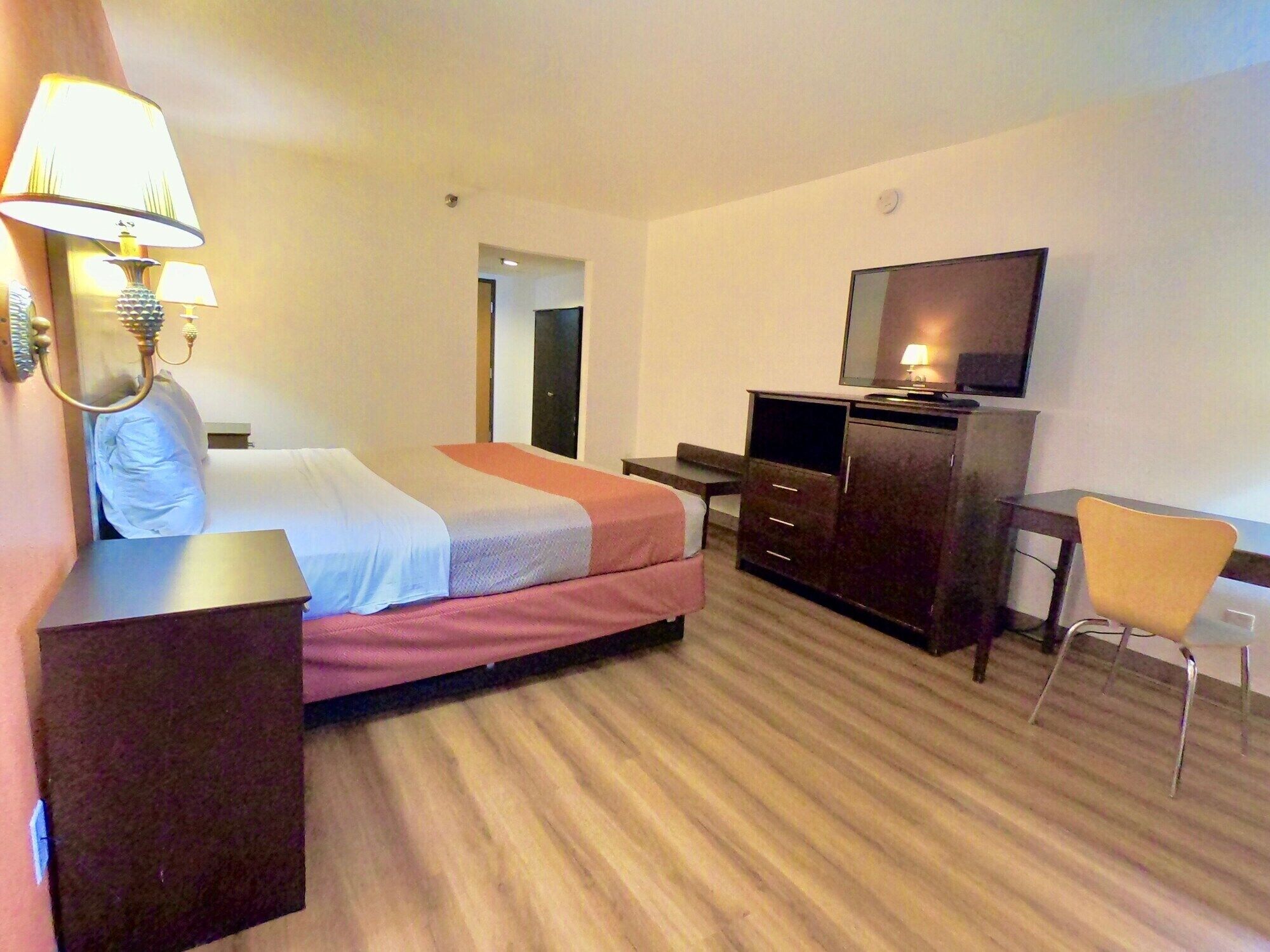 A hotel room with a bed, a desk, a chair, a TV, and a lamp.