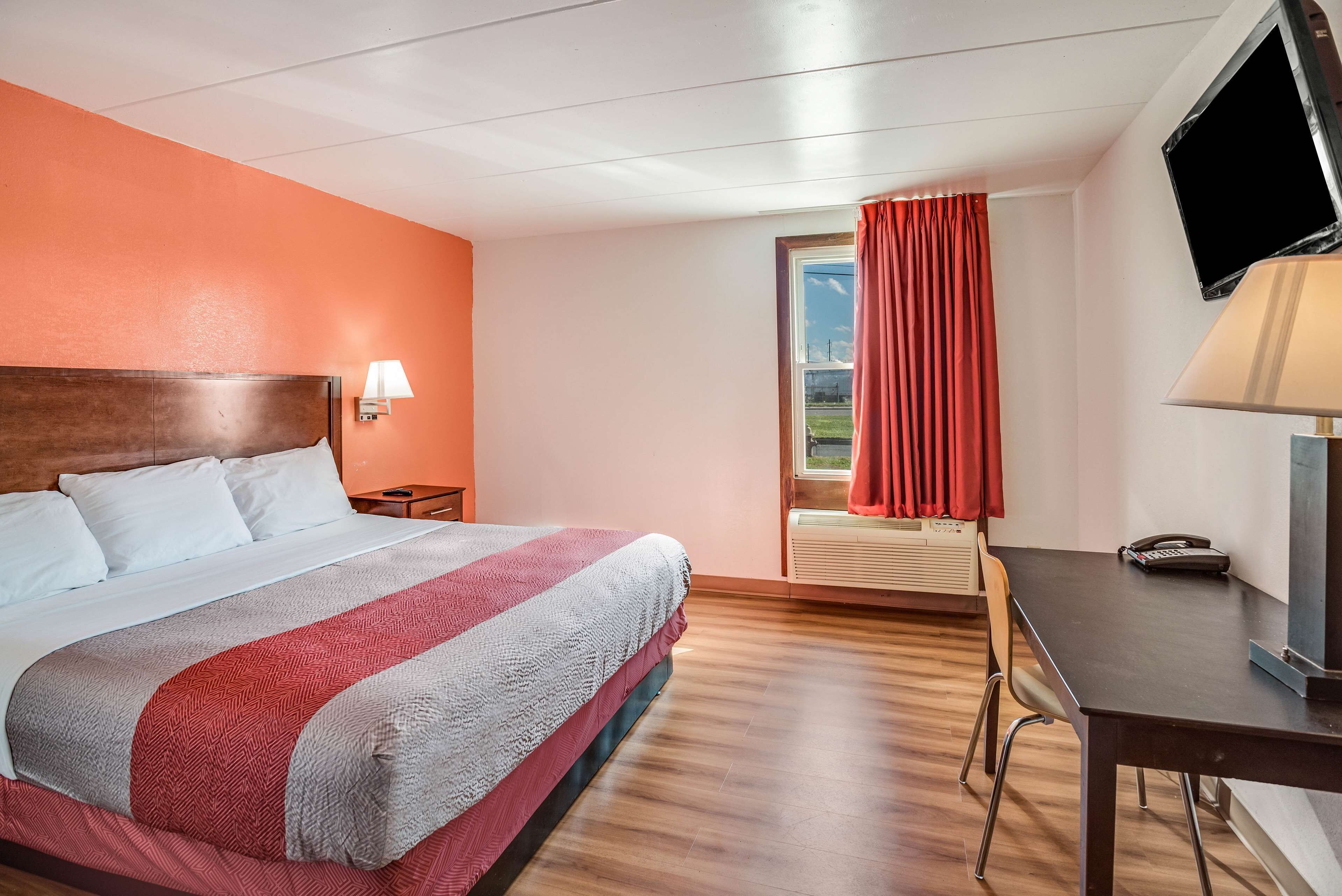 A hotel room with a bed, a desk, a chair, a TV, and a window with curtains.