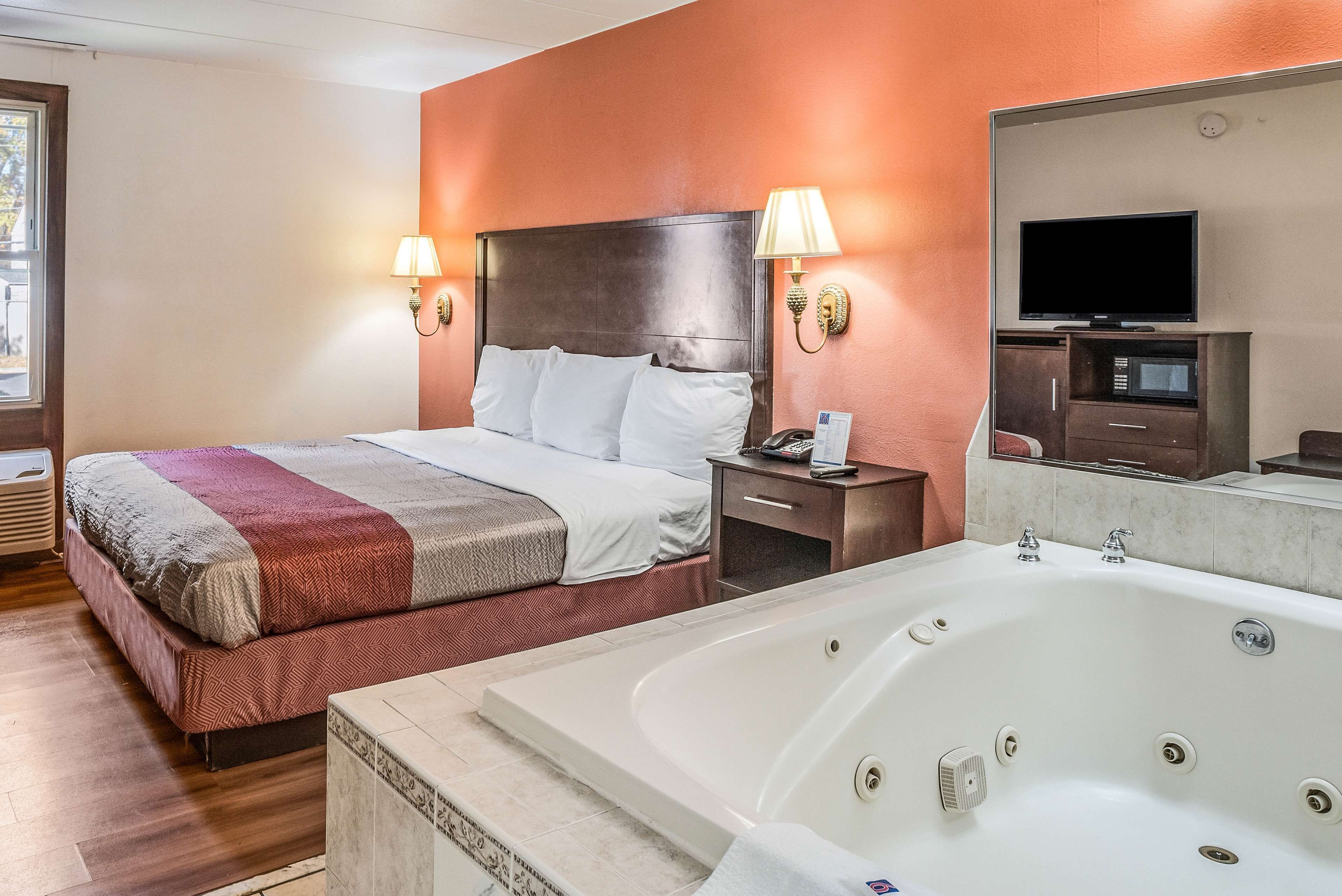 Une chambre d’hôtel avec un grand lit, un coin salon, une télévision, un minibar et une baignoire.