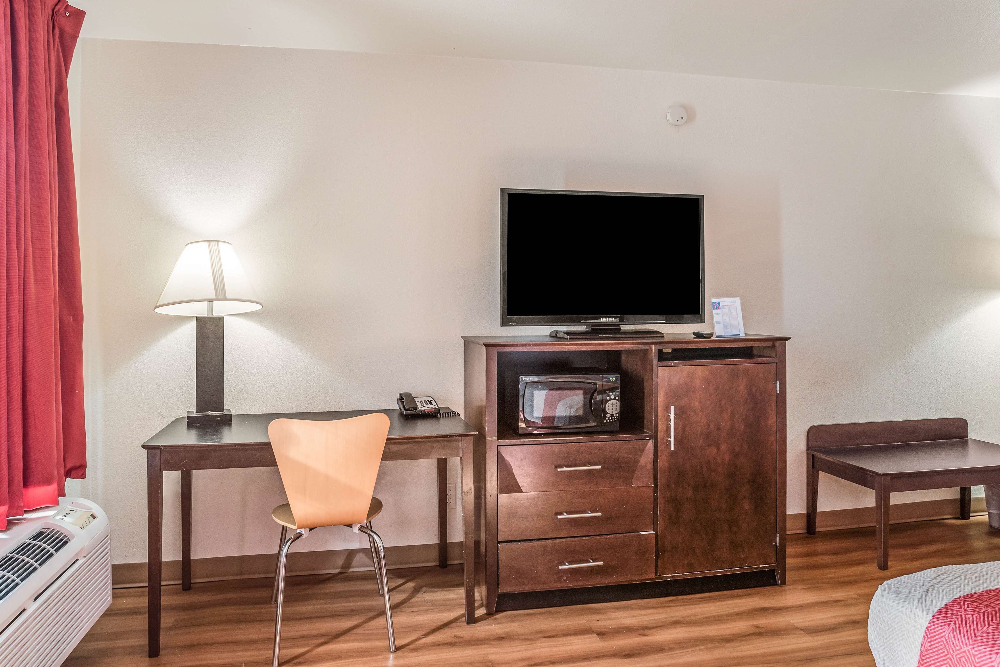 Una habitación de hotel con un escritorio de madera, un televisor, un microondas, una silla y una cama.