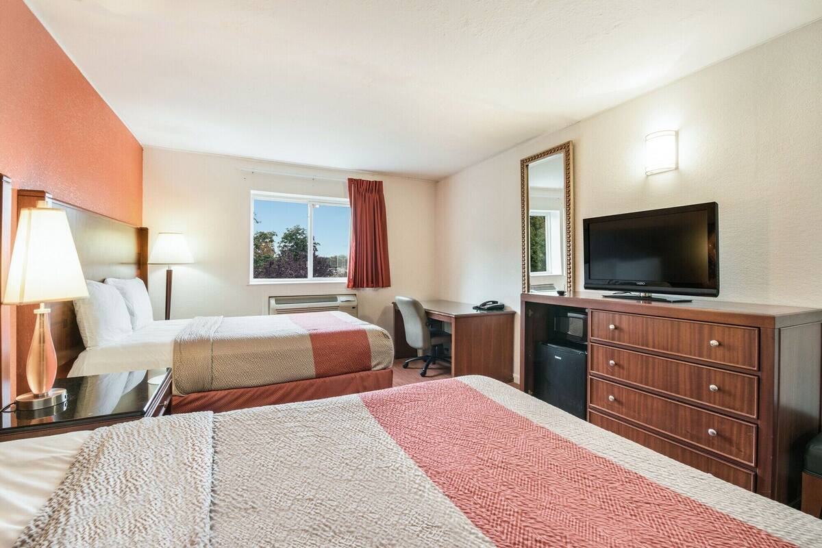Ein Hotelzimmer mit zwei Betten, einem Schreibtisch, einem Fernseher und einem Schminktisch.