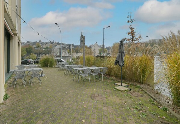 An outdoor patio area with tables and chairs, a street lamp, and a view of a town with buildings and a tower.