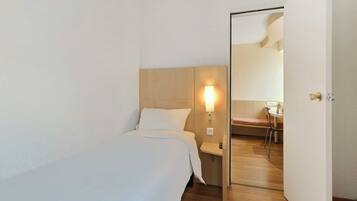 A hotel room with a bed, bedside table, lamp, and a mirror on the door.