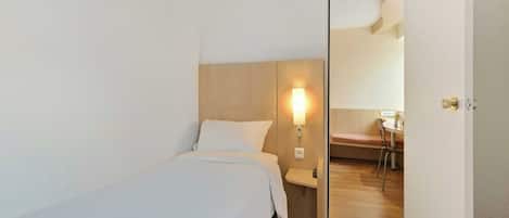 Una habitación de hotel con cama, mesita de noche, lámpara y espejo en la puerta.