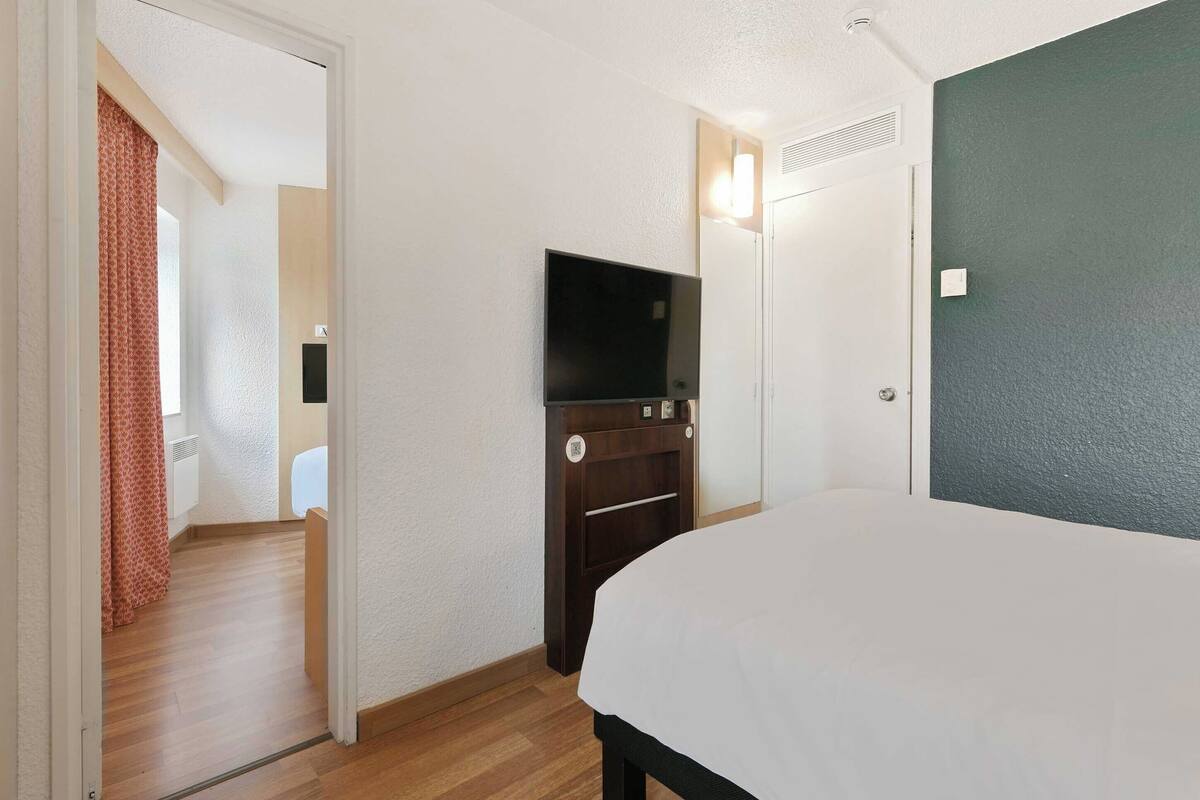 A hotel room with a bed, a TV, a wardrobe, and a door leading to another room.