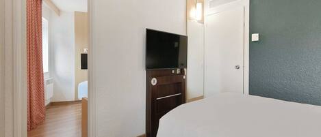 A hotel room with a bed, a TV, a wardrobe, and a door leading to another room.
