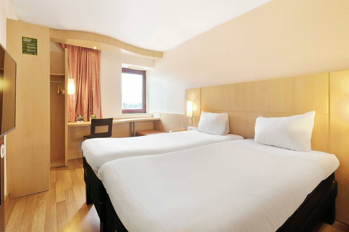 A hotel room with two beds, a desk, and a window with curtains.