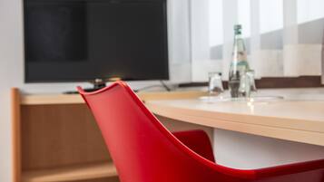 A modern room with a wooden desk, a red chair, a flat-screen TV, and a bottle of water on the desk.