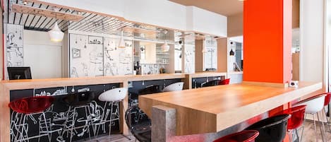 A modern bar area with a wooden counter, red and black bar stools, and a wall with artistic sketches.
