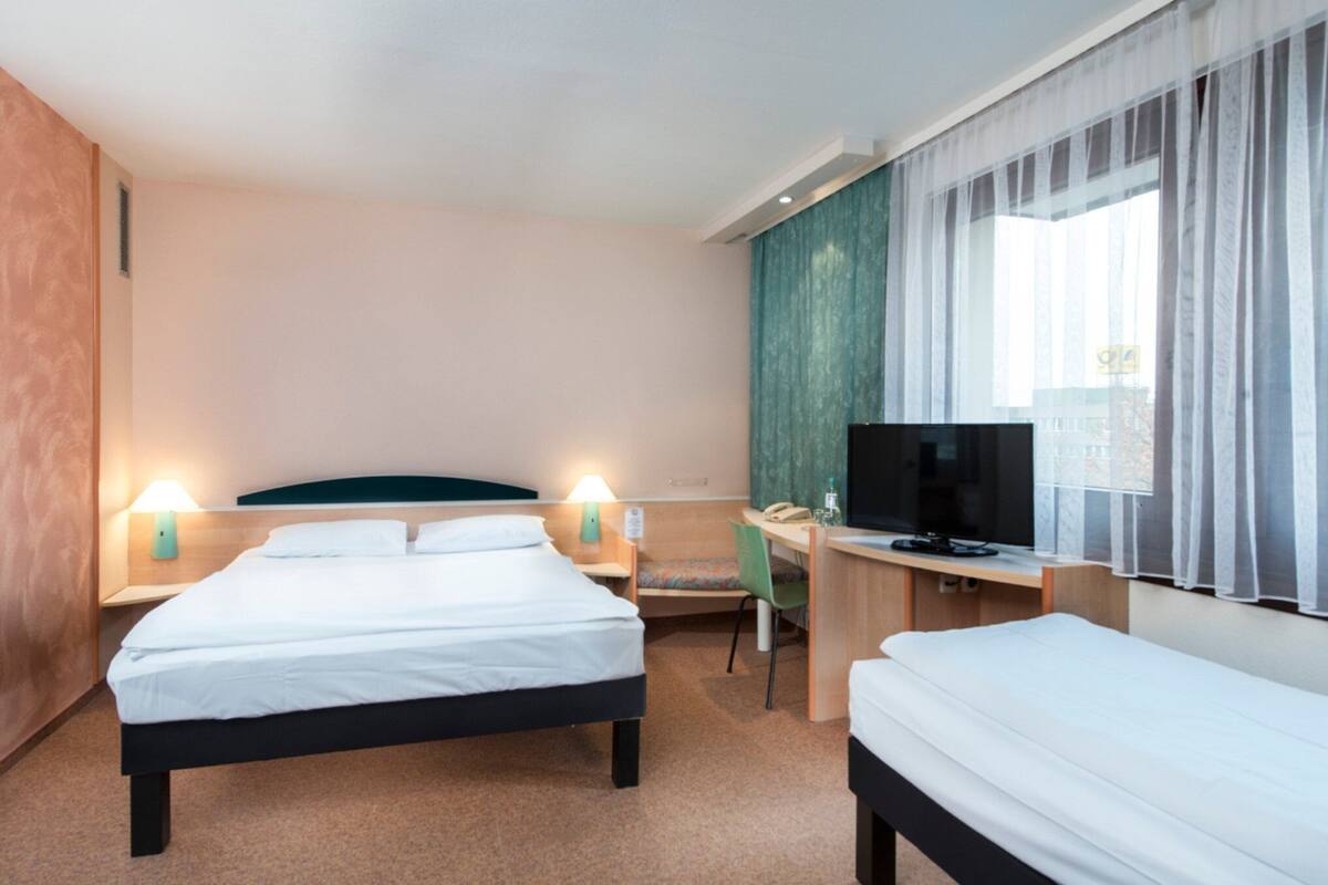 A hotel room with two beds, a desk, a chair, a TV, and two bedside lamps.
