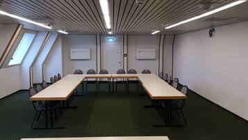 A conference room with a long table, chairs, ceiling lights, and air conditioning units.